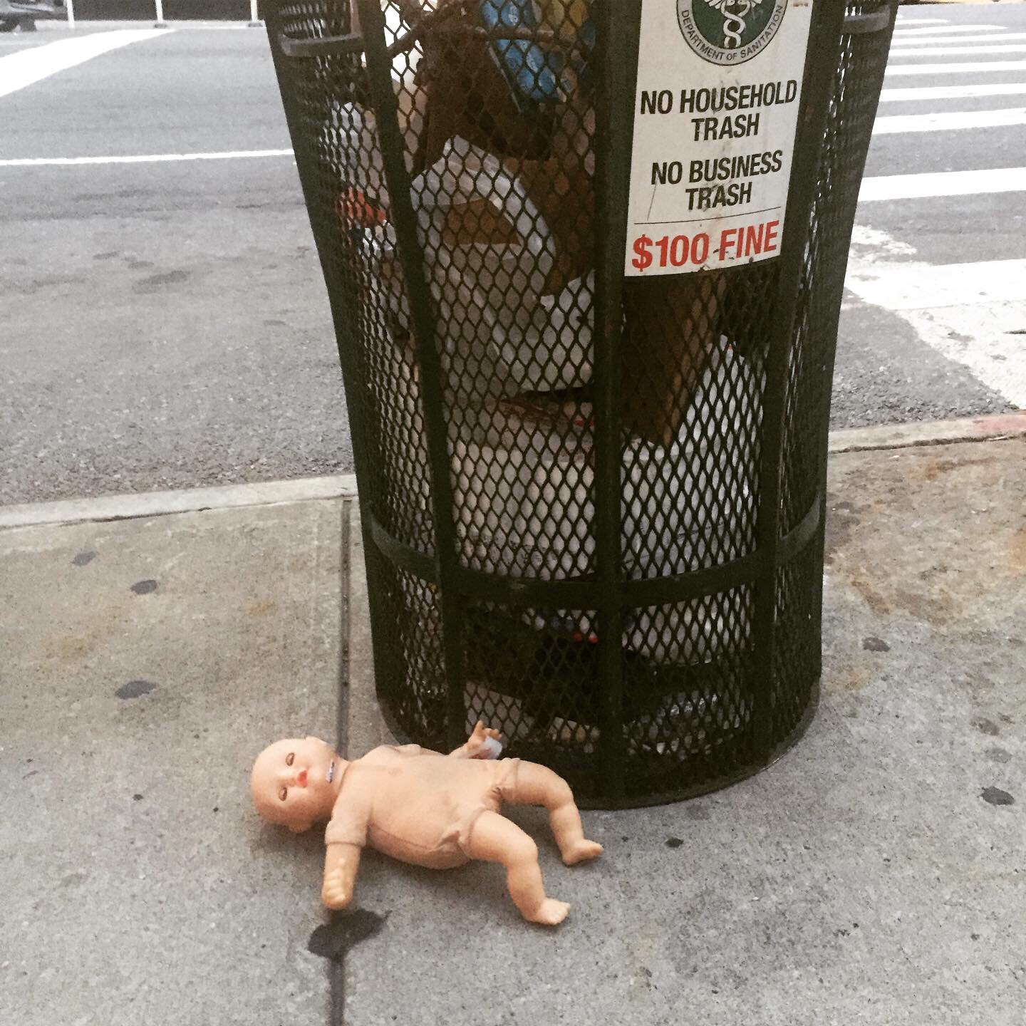 Abandoned baby doll next to NYC trash can.