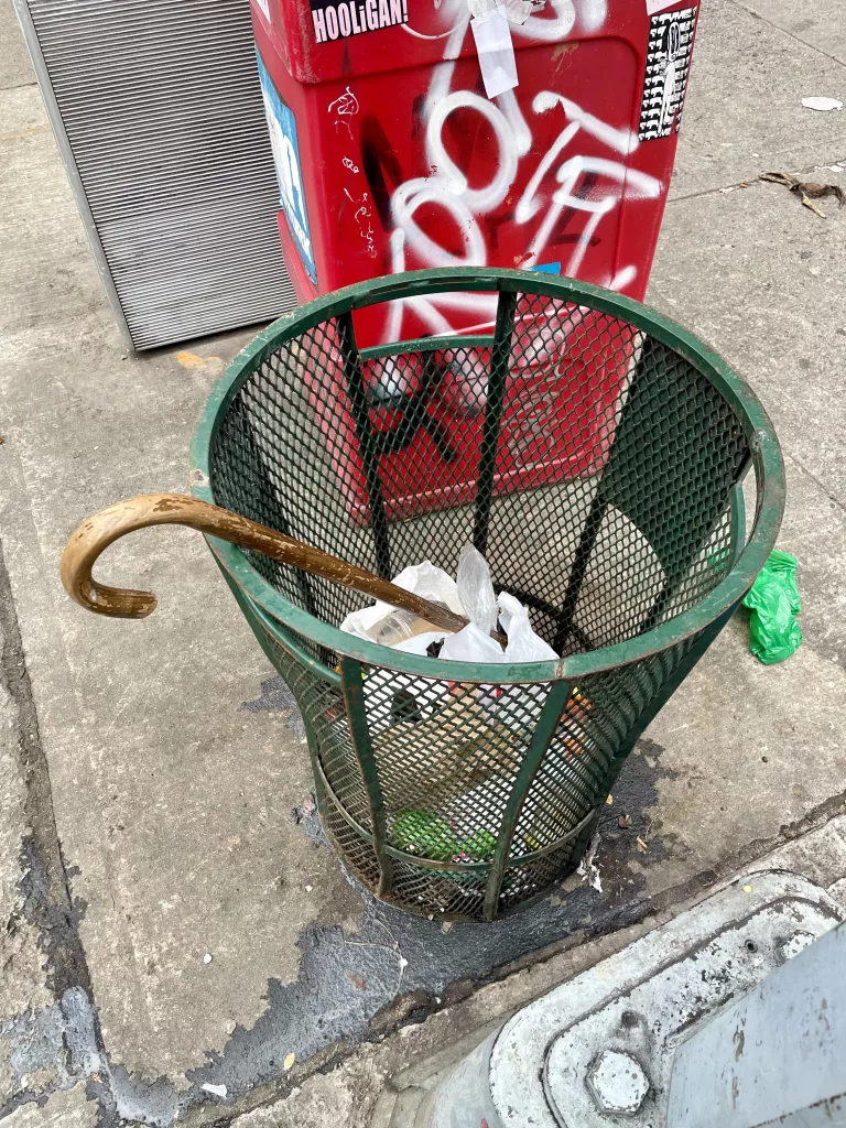 Wooden cane in a New York City street trash can.